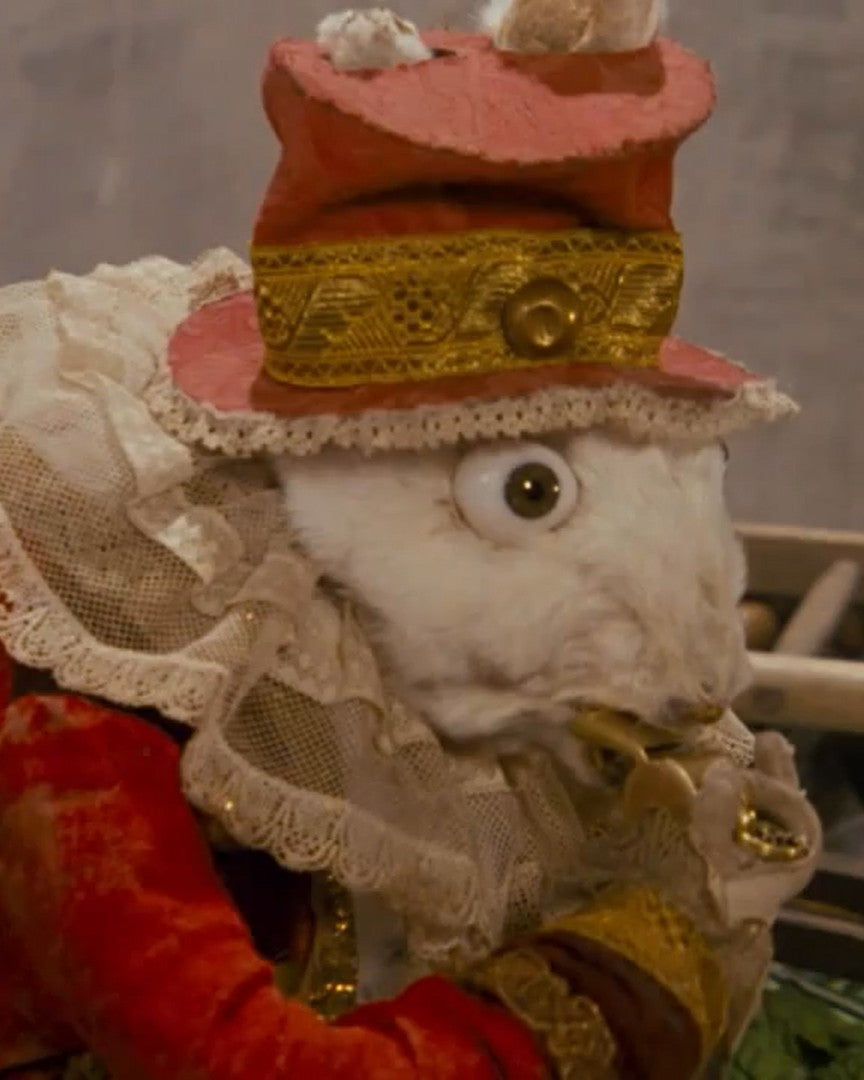 Decorative figure with a red hat and lace details, holding a small object.