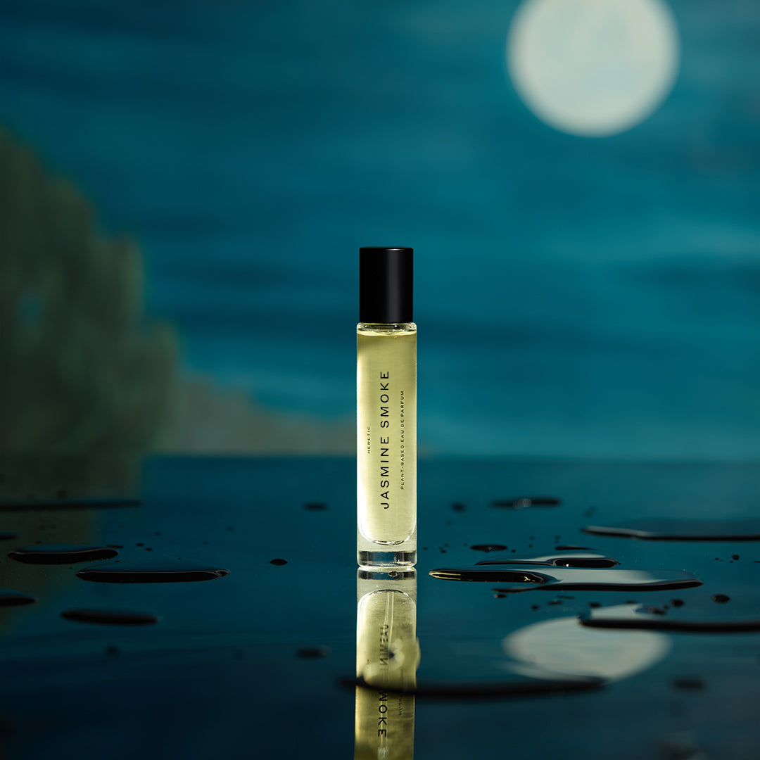 Perfume bottle labeled 'Jasmine Smoke' on a reflective surface with a blurred natural background