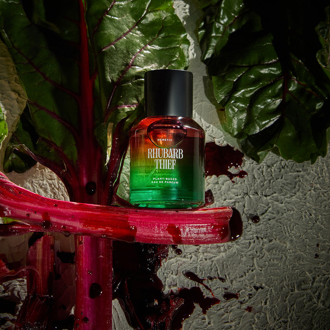 Bottle of Rhubarb Thief perfume on a red surface with green leaves in the background