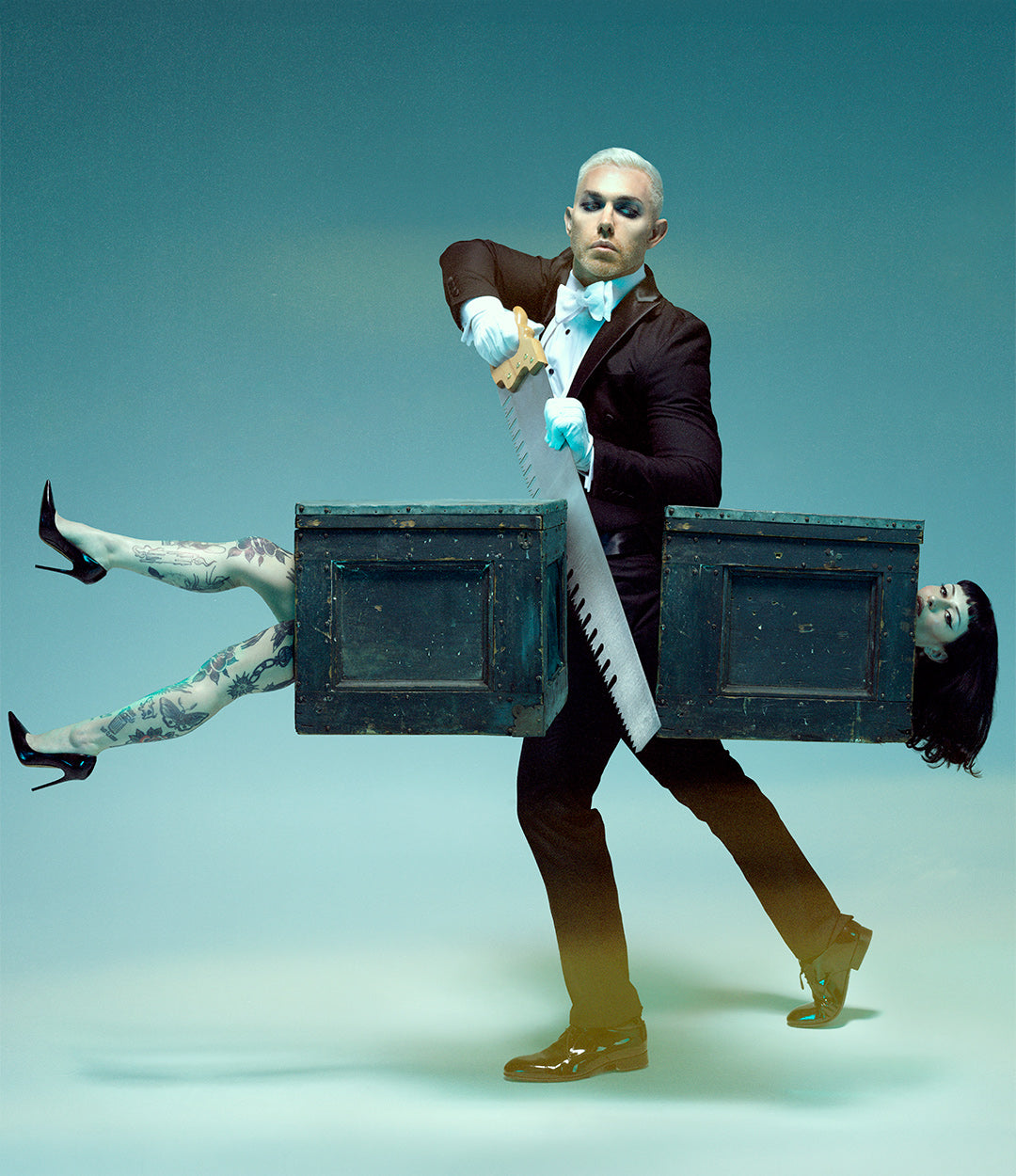 A surreal studio photograph of a man doing a magic trick of sawing a woman (Mars) in half while she's in a crate with legs and head sticking out.